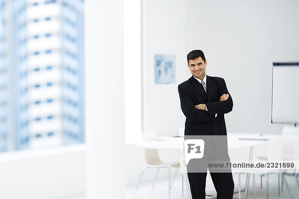 Businessman standing in meeting room with arms crossed  smiling at camera