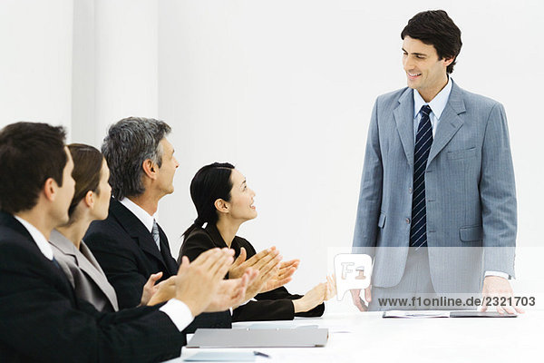 Group of business associates applauding colleague during meeting