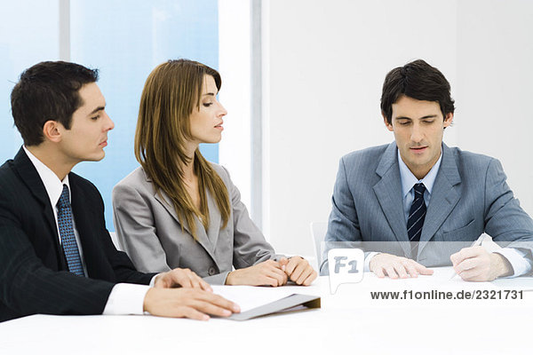 Business associates in meeting  man signing document while others watch