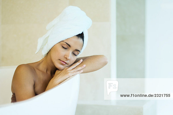 Frau in der Badewanne sitzend mit Handtuch um die Haare gewickelt  Kopf auf den Armen ruhend  Augen geschlossen