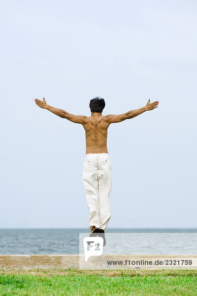 Mann springt am Strand in die Luft  Arme ausgestreckt  Rückansicht