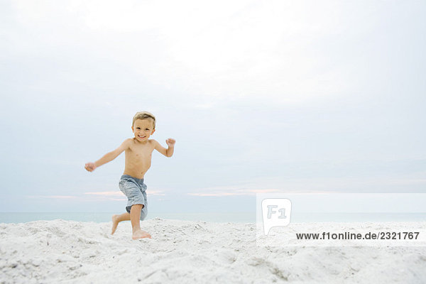 Kleiner Junge rennt am Strand  lächelt in die Kamera.