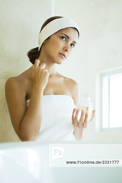 Junge Frau in Handtuch gewickelt  Parfüm auf den Hals auftragend  wegschauend
