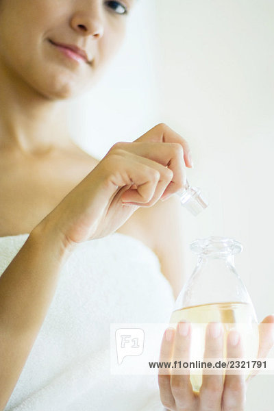 Frau in Handtuch gewickelt  Parfümflasche öffnend  lächelnd in die Kamera  Ausschnittansicht