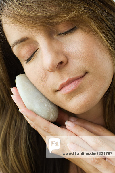 Frau hält glatten Stein gegen die Wange  Augen geschlossen  Nahaufnahme