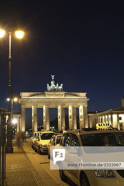 Taxis near memorial gate lit up at dusk  Brandenburg Gate  Berlin  Germany