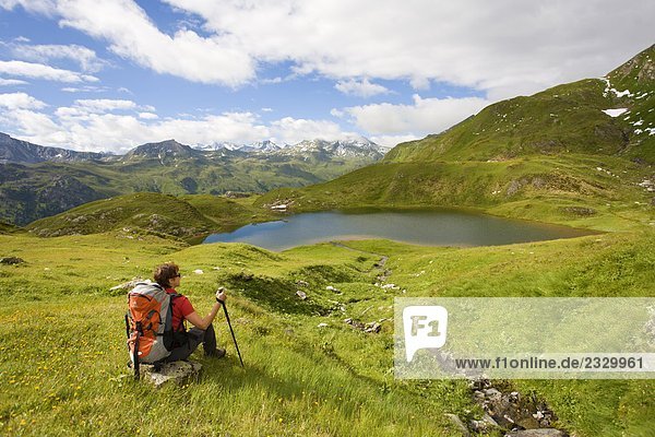 Rear view of hiker sitting on rock in field Hohen Tauern Salzburg Austria
