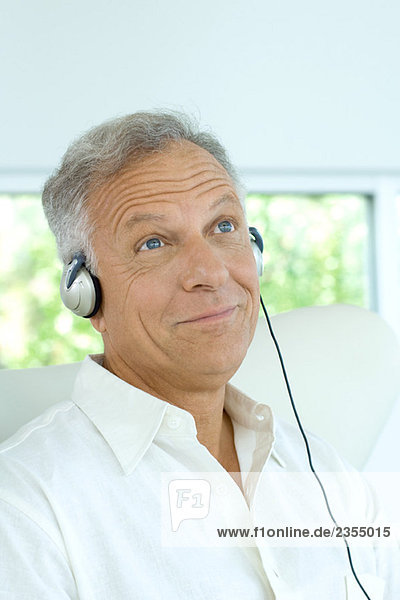 Mature man listening to headphones  smiling  looking up