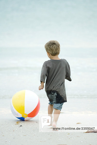 Kleiner Junge jagt Strandball am Strand  Rückansicht