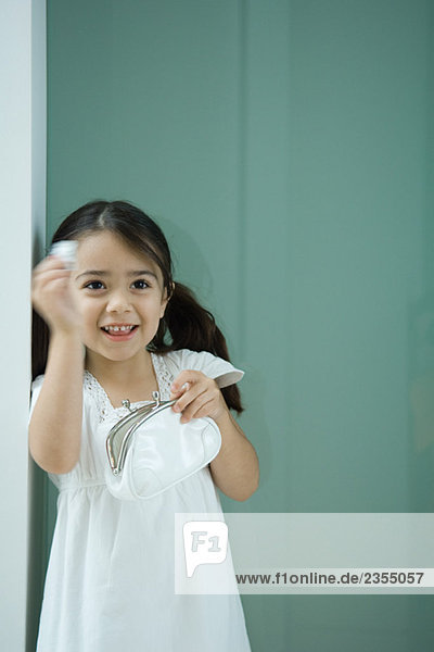 Kleines Mädchen mit Geldbörse  eine Hand erhoben  lächelnd