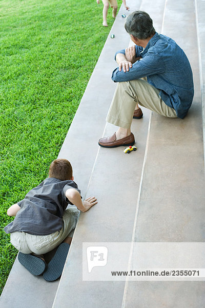Großvater und Enkelkinder sitzen auf einer Treppe  spielen mit Spielzeugautos  hohe Blickwinkel
