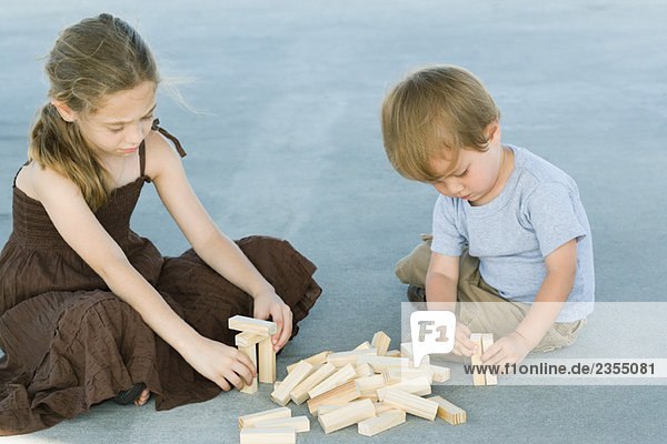 Bruder und Schwester sitzen auf dem Boden und spielen mit Bausteinen zusammen.