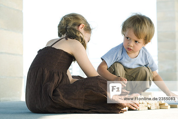 Junge und Mädchen sitzen auf dem Boden und spielen mit Bausteinen.