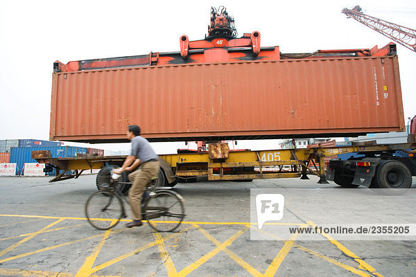 Mann auf dem Fahrrad  vorbei an LKW und Stauraum aus Metall  Seitenansicht
