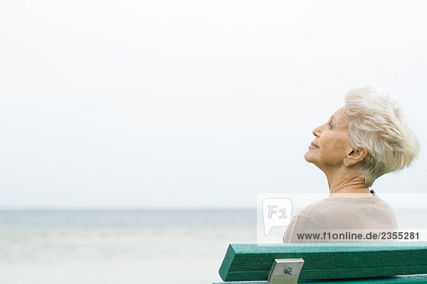 Seniorin am Meer sitzend  mit Blick auf die Aussicht