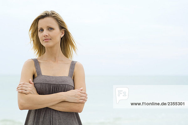 Blonde Frau stehend mit gefalteten Armen  Meer im Hintergrund  Blick auf Kamera  Taille oben