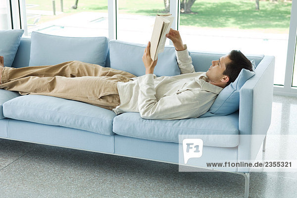 Man lying on sofa  reading book  side view