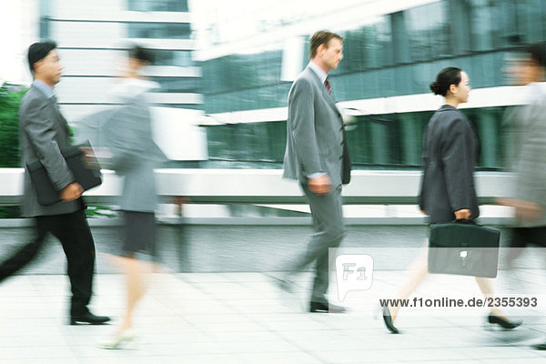 Male and female professionals walking on sidewalk  blurred motion