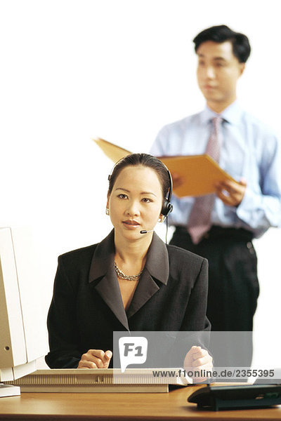 Geschäftsfrau am Schreibtisch sitzend  Kopfhörer tragend  wegschauend