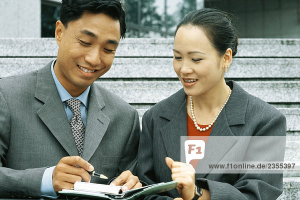 Male and female business associates looking at agenda together  smiling  man holding pen