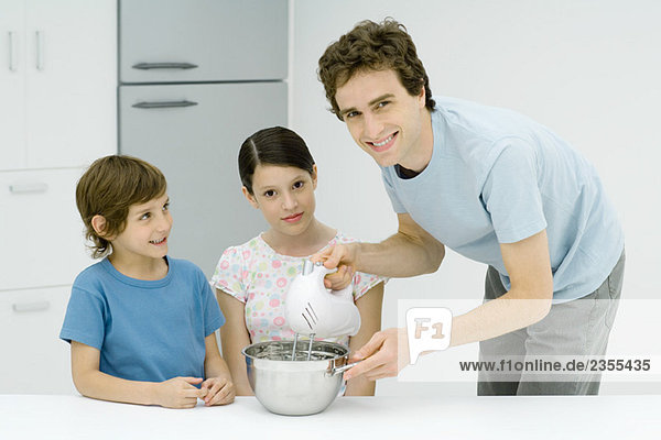 Mann beim Kochen mit Mädchen und Junge  lächelnd vor der Kamera