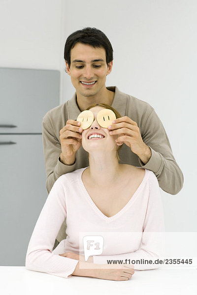 Junges Paar in der Küche  Mann hält Obstscheiben vor den Augen der Frau