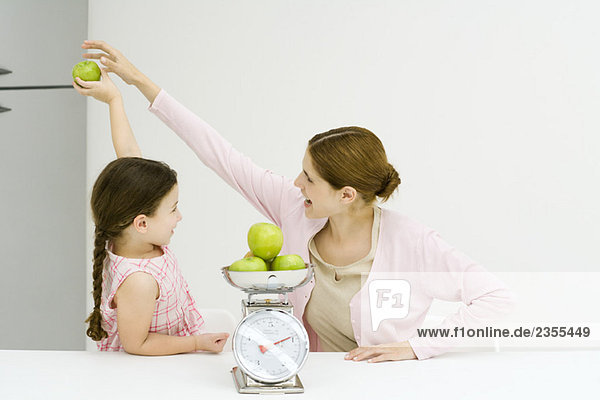 Frau und Mädchen  Mädchen hält den Apfel hoch  Frau greift danach.