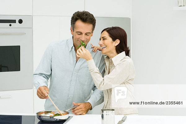 Man cooking  woman holding up basil for man to smell