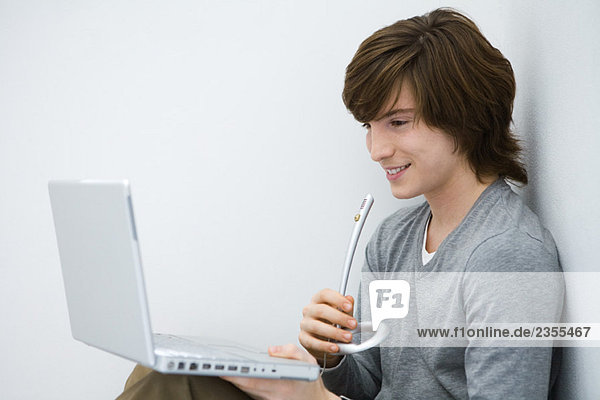 Young man looking at laptop computer  speaking into microphone  side view