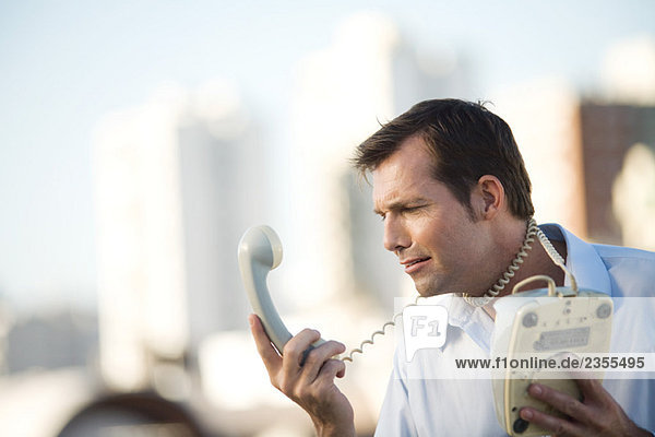 Man wrapping landline phone cord around neck  looking at receiver