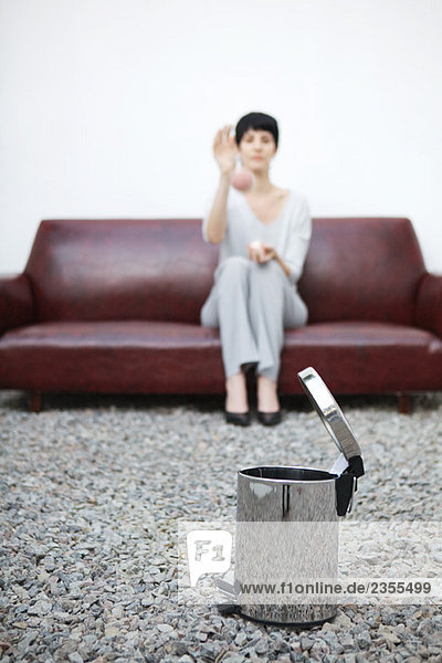 Woman sitting on sofa  throwing ball at garbage can in foreground