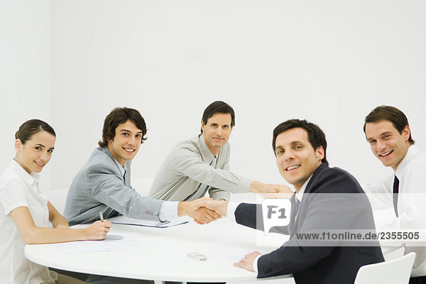 Business associates shaking hands across table  smiling at camera