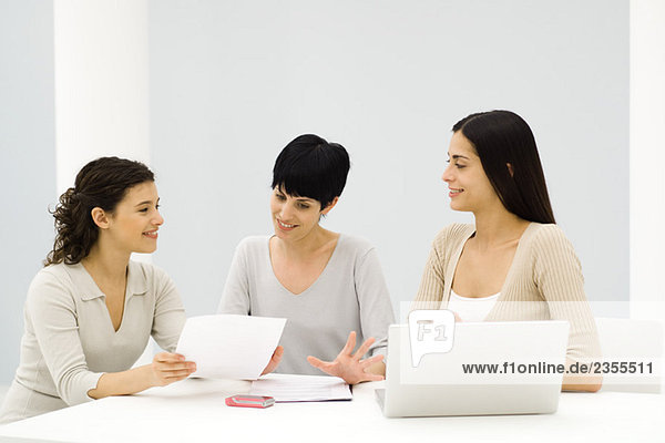 Three female professionals sitting at table  having discussion  one holding document