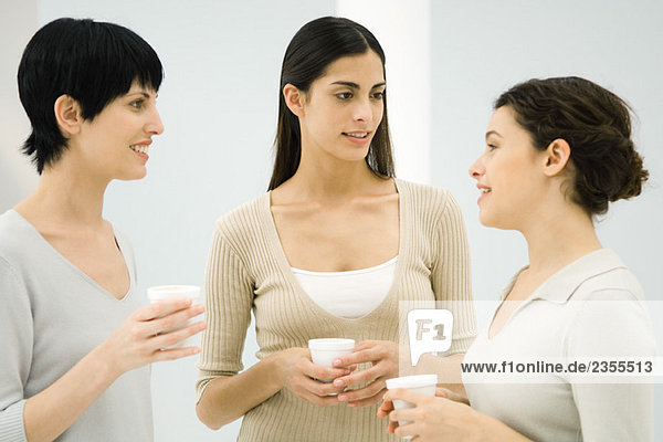 Drei Frauen im Gespräch  alle mit Einweg-Kaffeetassen.