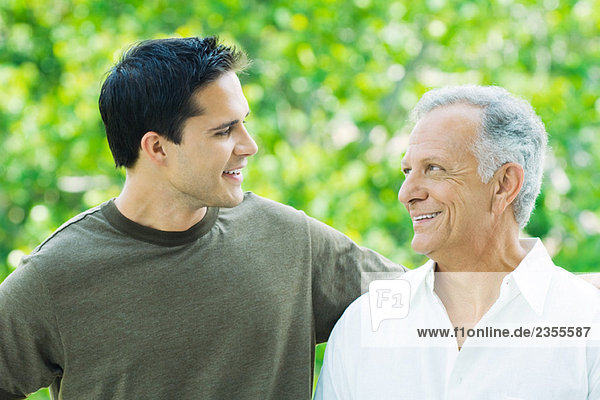 Mature man and adult son looking at each other  smiling