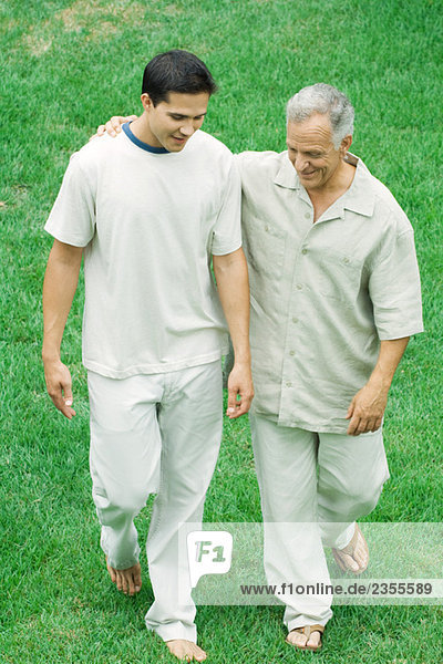 Mature man walking with arm around adult son's shoulder outdoors  both looking down