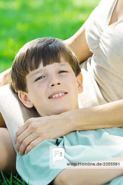 Boy resting head on mother's lap  smiling at camera  close-up