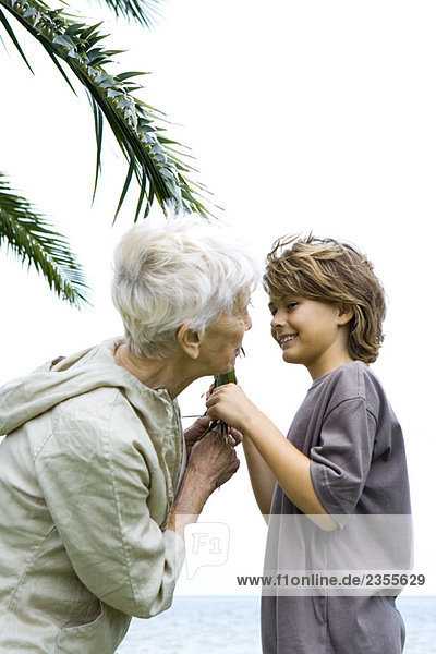 Großmutter und Enkel stehen sich gegenüber  halten Palmblatt und lächeln sich an.