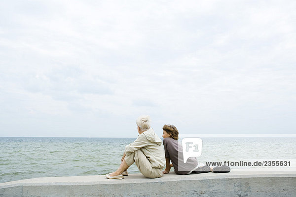 Großmutter und Enkel sitzen zusammen am Meer  Blick auf das Meer  Rückansicht