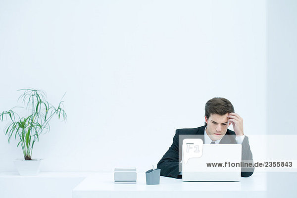 Man sitting at desk  using laptop  holding head