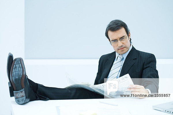 Geschäftsmann sitzend mit erhobenen Füßen  Zeitung lesend