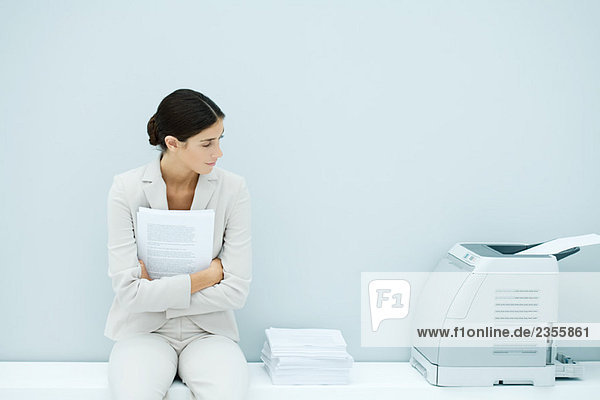 Junge Frau im Anzug sitzend neben dem Drucker
