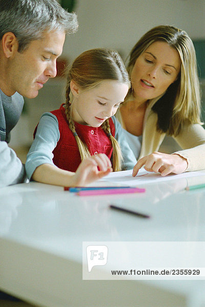 Little girl doing homework with parents