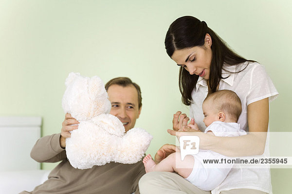 Mother holding infant on lap  father holding teddy bear  smiling