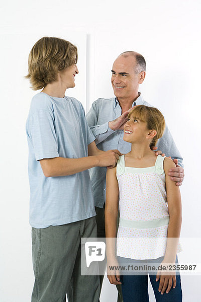 Father standing with teen son and preteen daughter  all smiling at each other