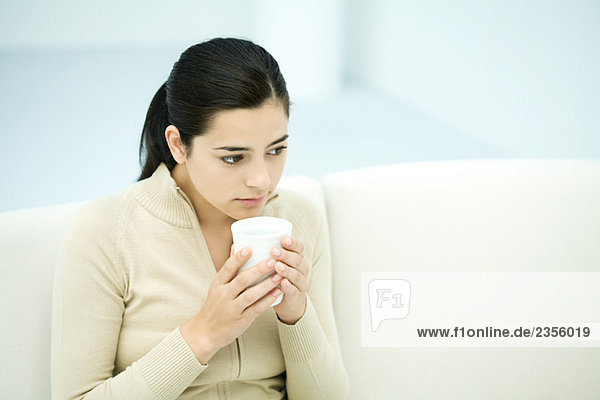 Junge Frau sitzend  Kaffeetasse haltend  wegschauend