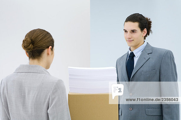 Young professionals standing face to face  documents stacked on cardboard box between them