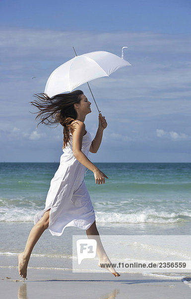 Frau mit Sonnenschirm am Strand überspringen