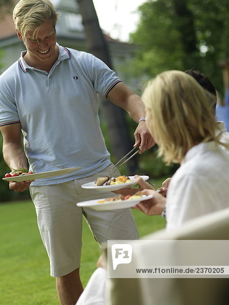 Mann mit Essen an seine Freunde auf einer Gartenparty