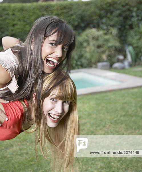 Woman outdoors giving other woman piggyback ride and smiling
